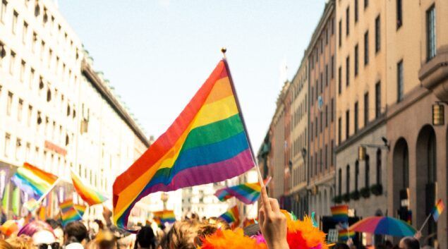 Rainbow flag waving in a crowd during a pride parade on a city street