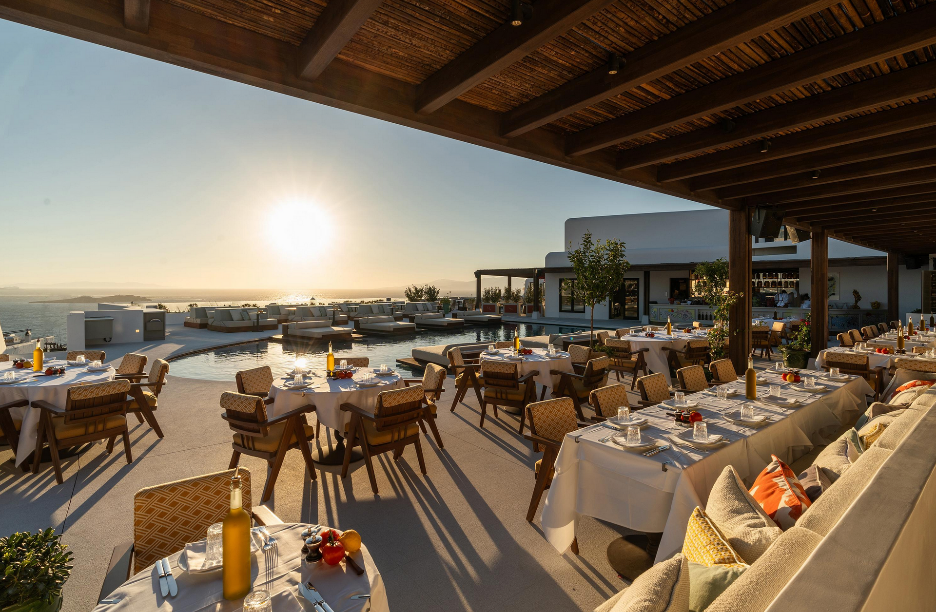 Restaurant patio with tables set for dining, ocean view at sunset. Elysium