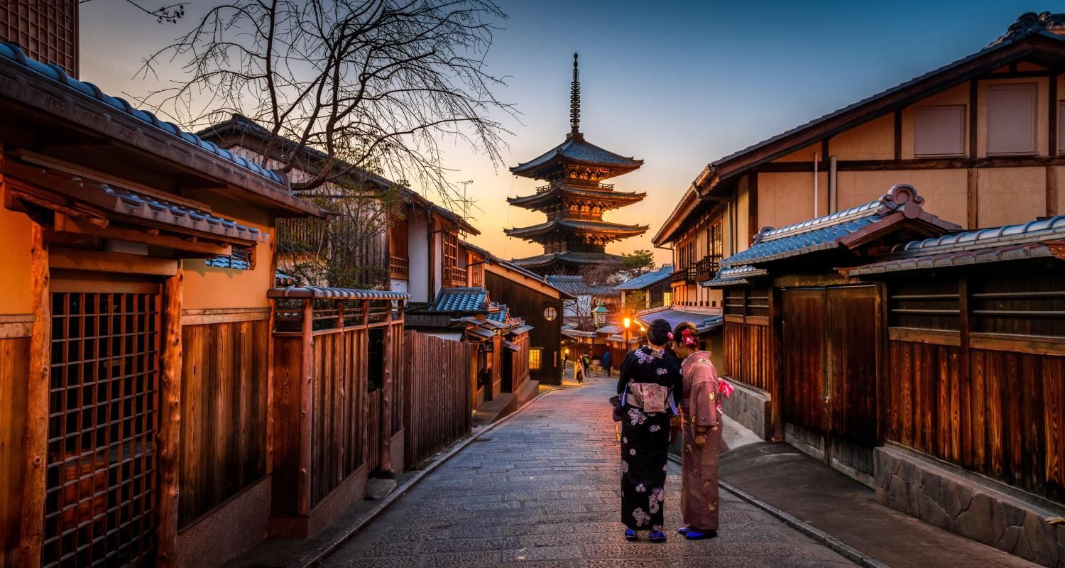 Two people in kimonos walk down a narrow, historic stone street in Kyoto, Japan, toward a traditional five-story pagoda.