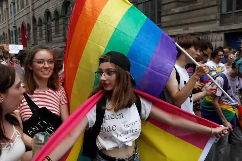 People at a Pride parade, one holding a rainbow flag, others smiling, marching on a street.