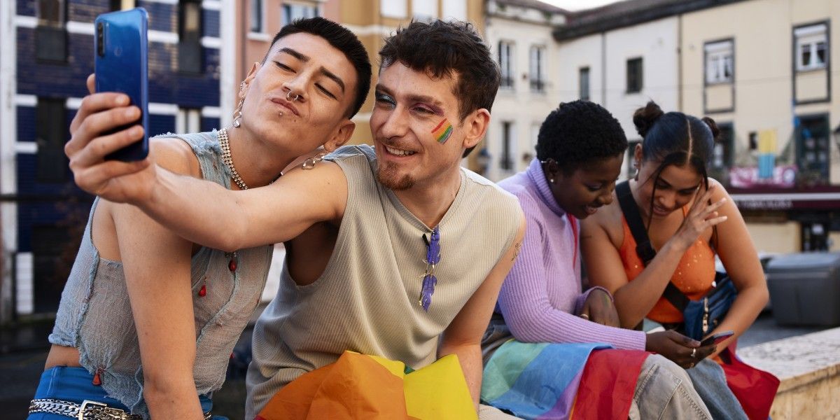 Two friends taking a selfie on city steps while others sit nearby and look at their phones