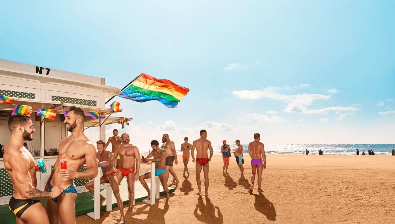 Beach scene with group of men in swimsuits near a bar with rainbow flags. Maspalomas