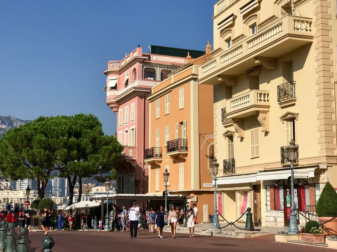 Buildings on a sunny street in Monaco with people walking by.