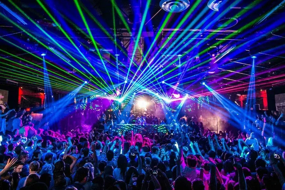 A crowded concert with colorful lasers, blue and pink lights, and people dancing.