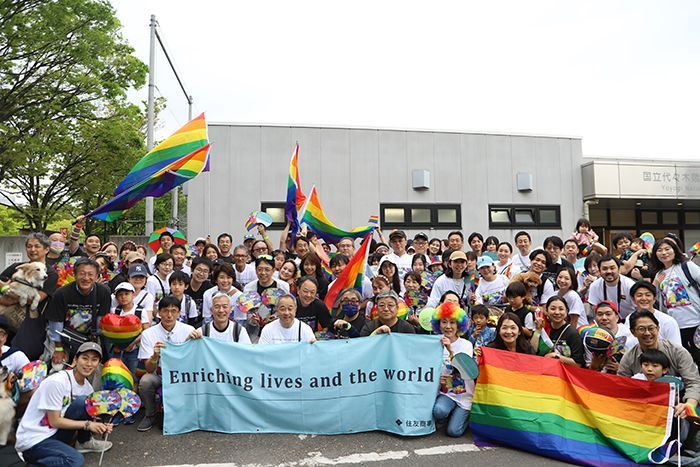 Group of people with Pride flags holding a banner that reads 