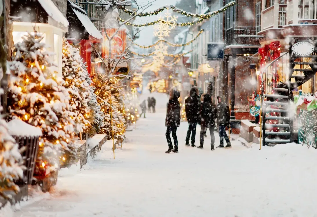 Snowy Christmas market street with lit trees and figures.