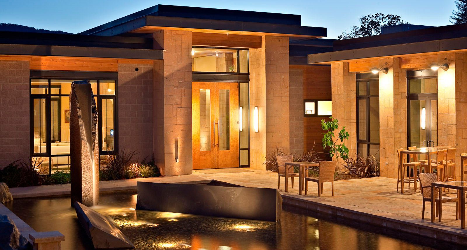 Modern building with illuminated facade, reflecting in water feature; outdoor seating.