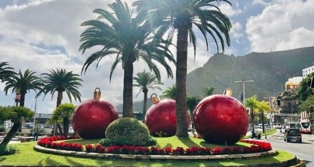 Giant red Christmas ornaments in a roundabout with palm trees, with mountains in the background. Gran Canaria