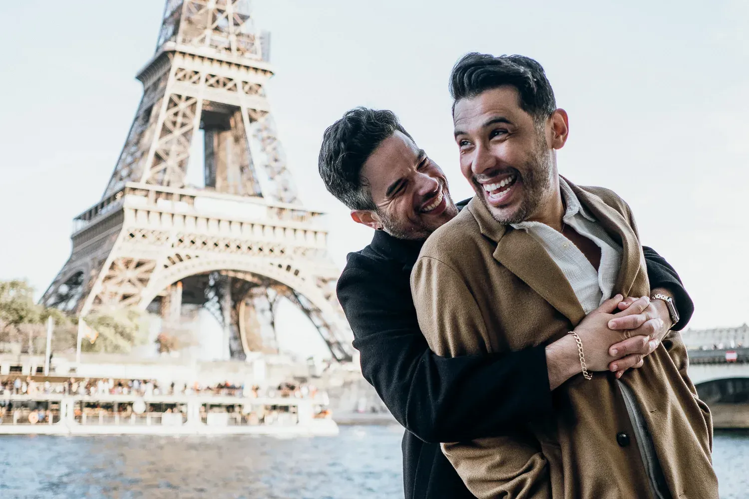 Two men embracing and laughing in front of the Eiffel Tower.