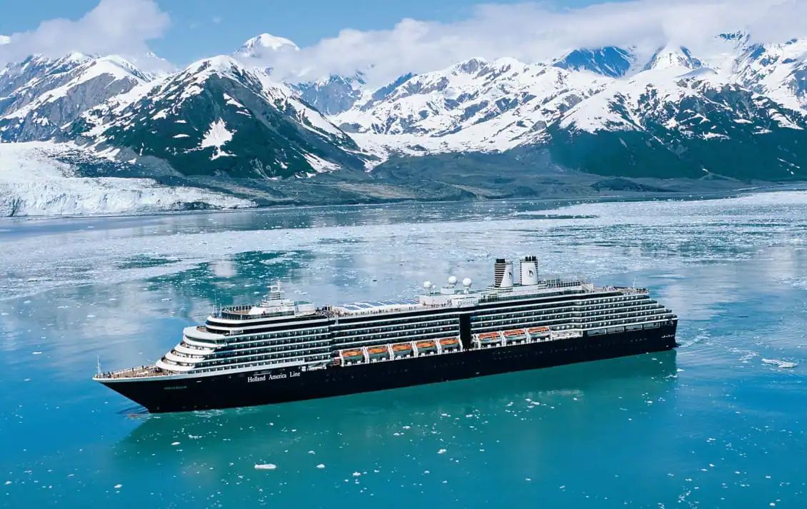 Cruise ship sailing in front of snow-capped mountains and a glacier.