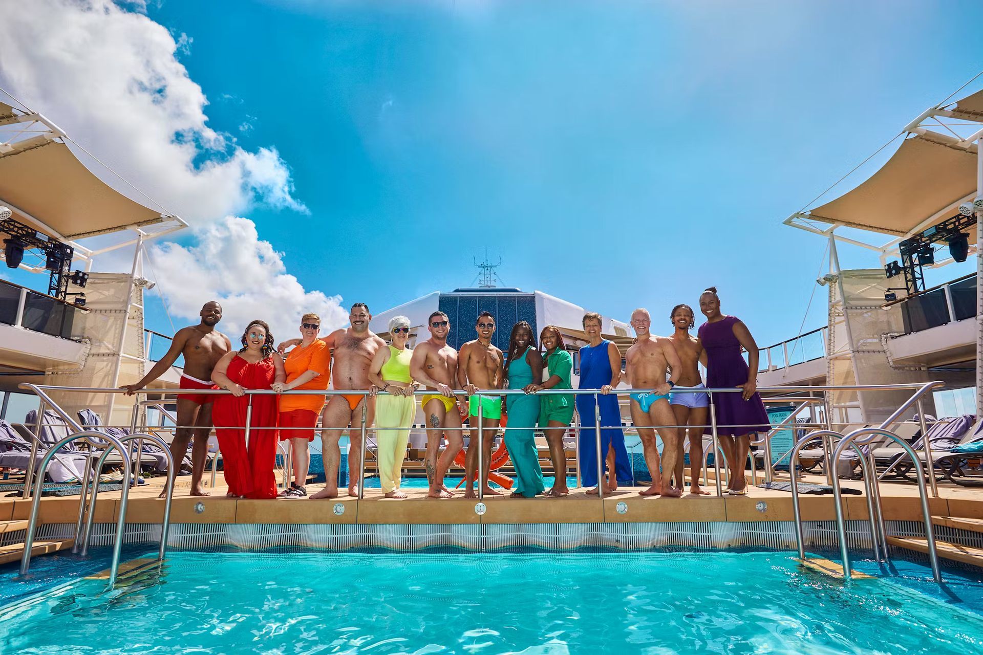 A group of people in colorful outfits pose by a pool on a cruise ship deck under a sunny sky. Caribbean