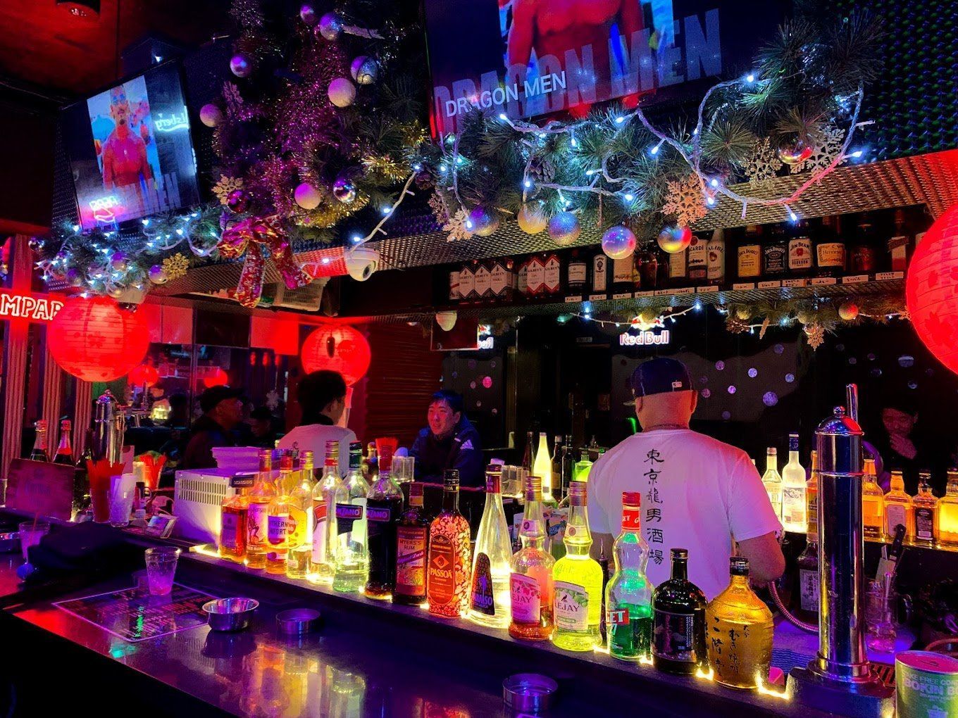 Bar interior with bottles, bartenders, and holiday decorations, with string lights and red lanterns. men-tokyo-gay-bar-main-1.jpg