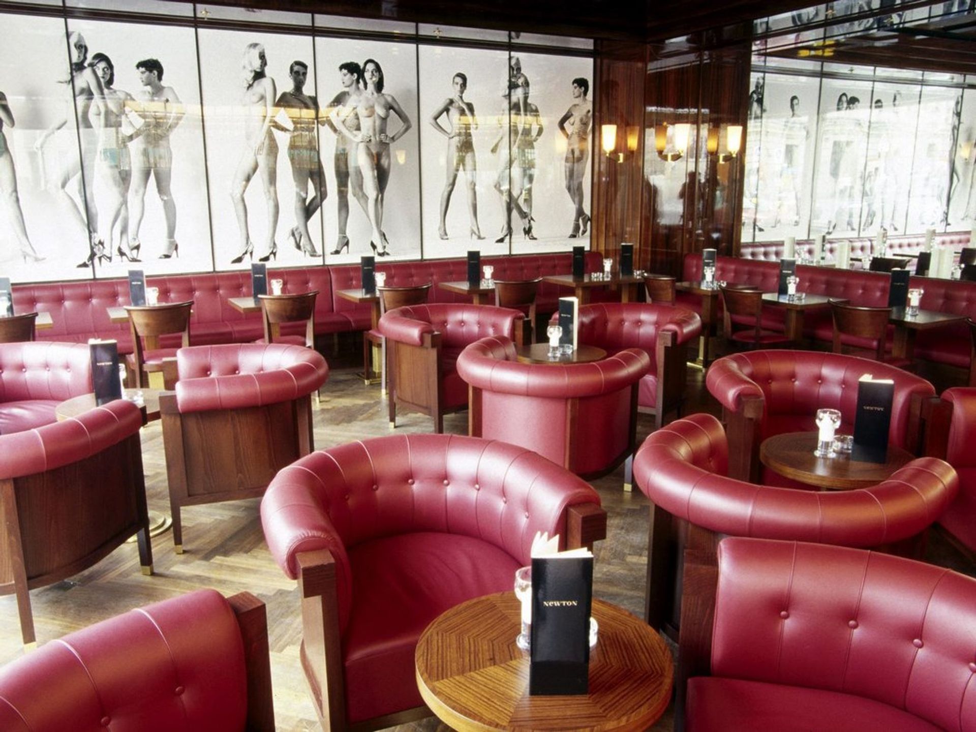 Red leather seating in a dimly lit bar with a large black and white mural of figures on the wall.