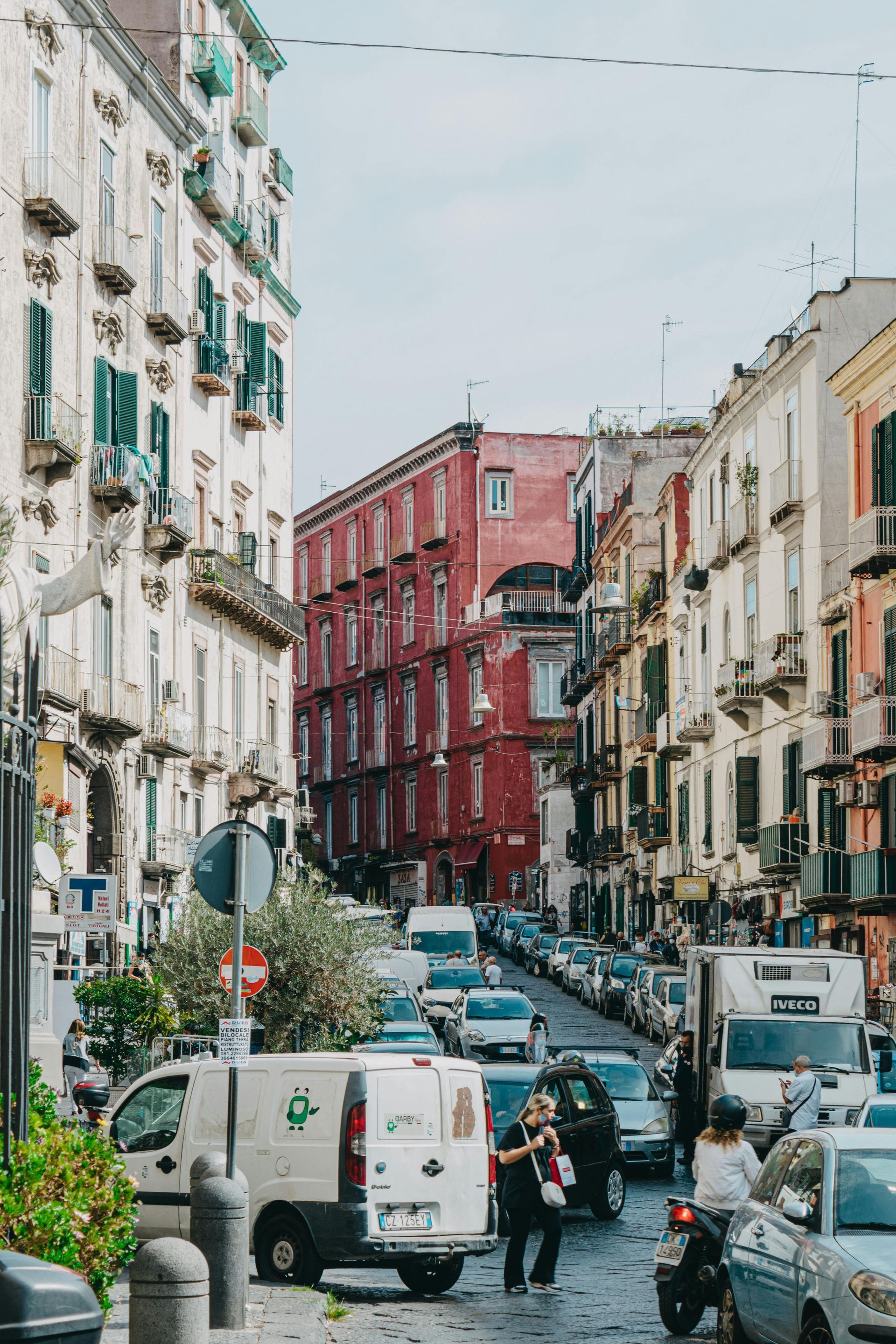 Narrow street in Naples with colorful buildings and parked cars.