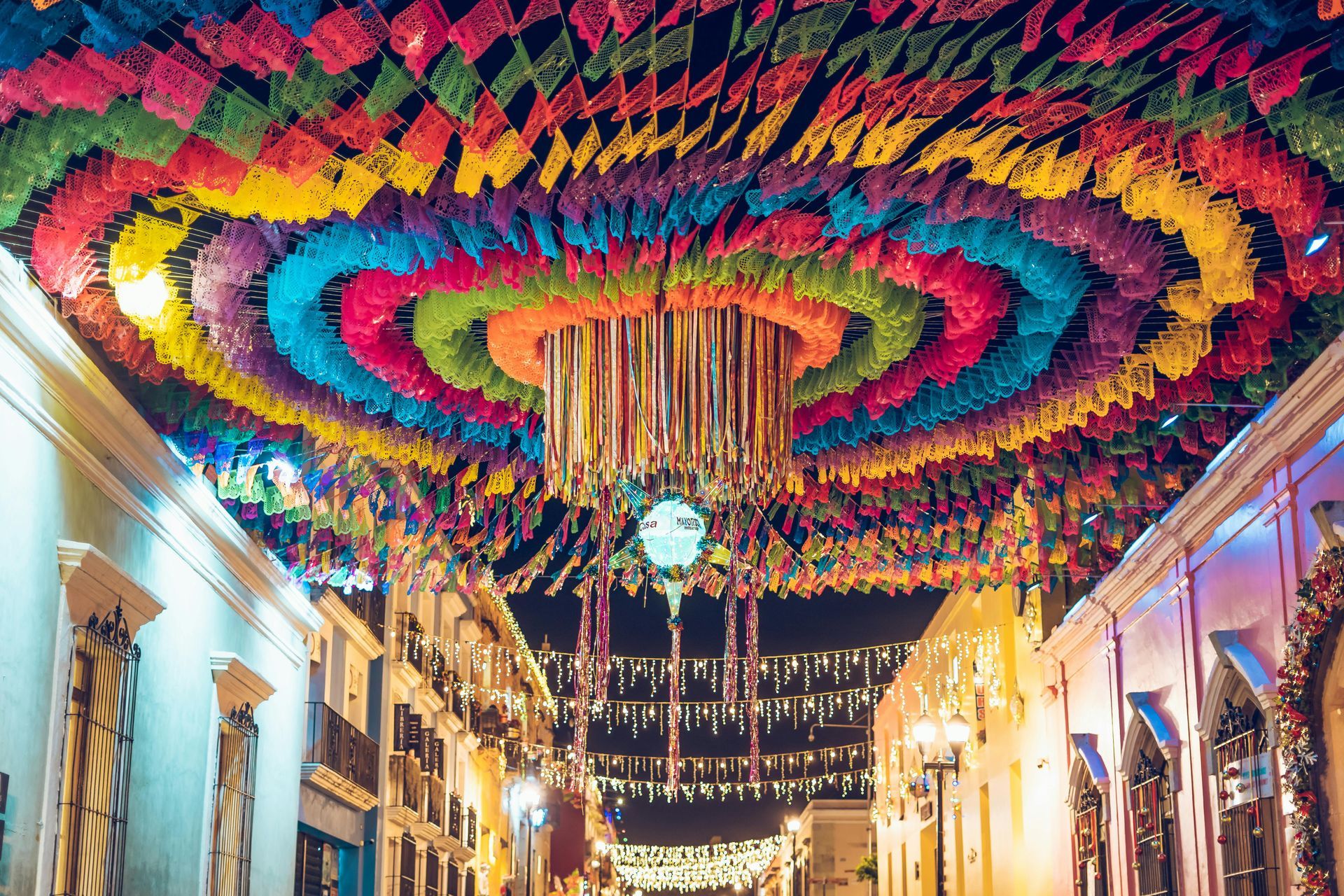 Colorful rainbow canopy of hanging decorations over a narrow street at night