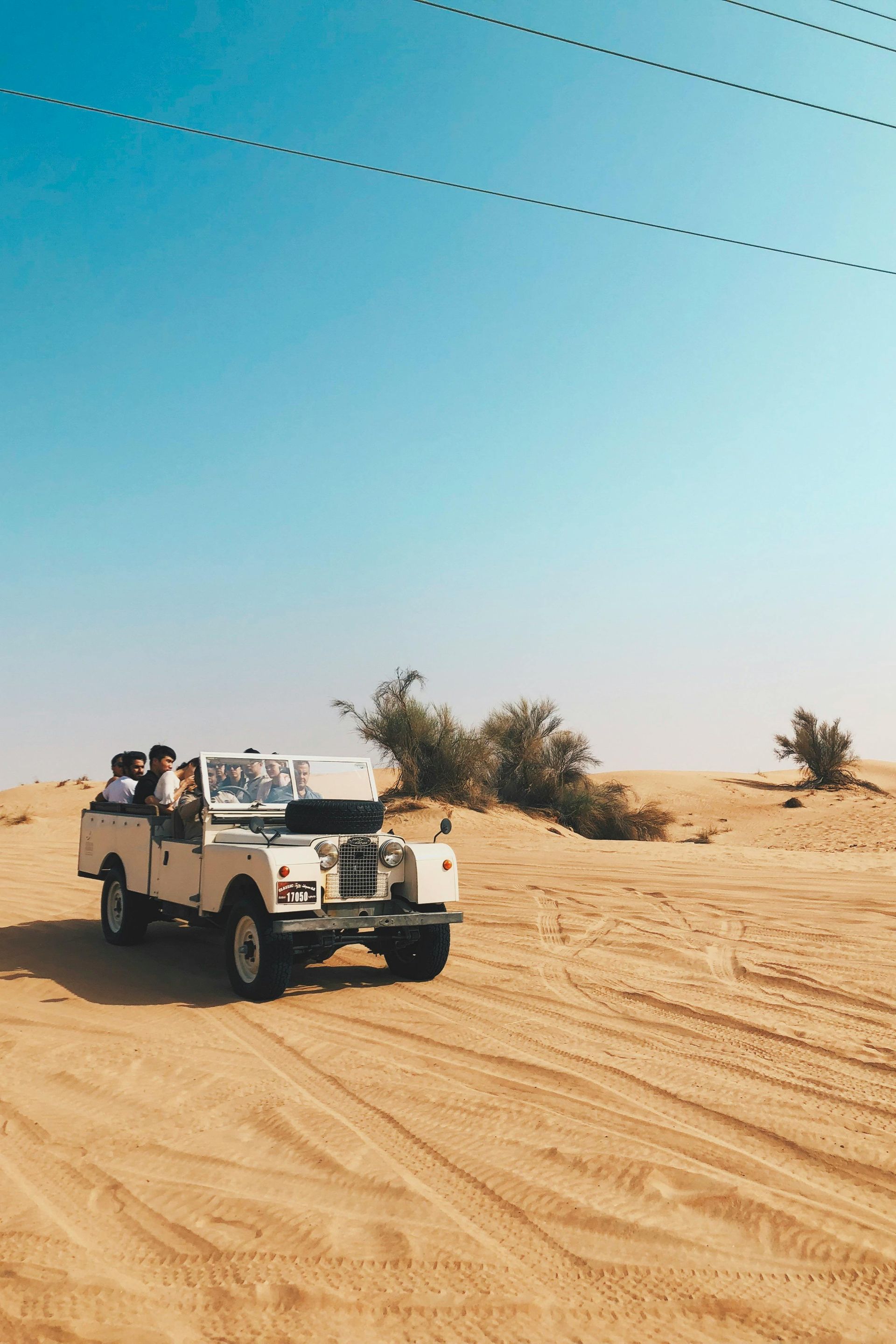 White safari vehicle driving through a sandy desert under a clear blue sky.