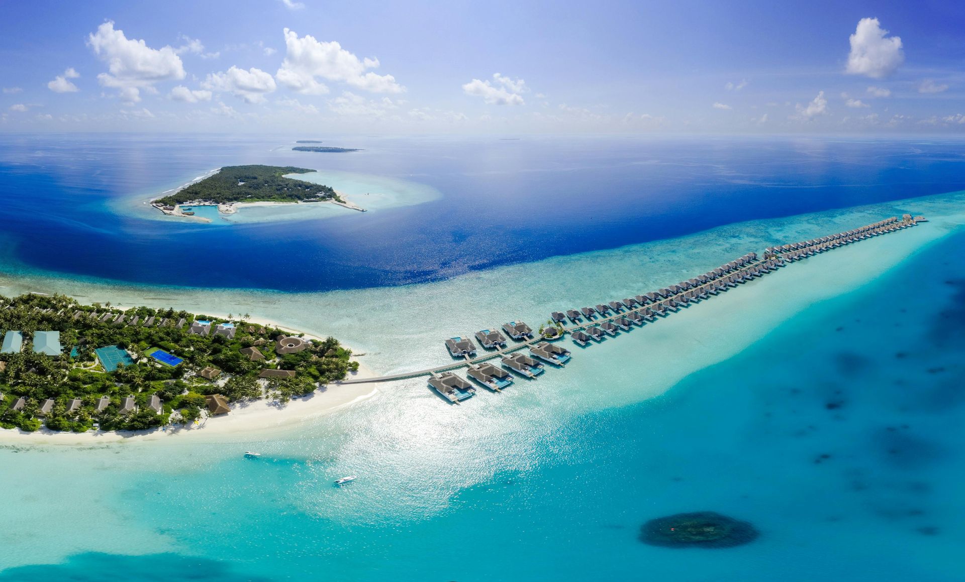 Aerial view of a tropical island with overwater bungalows and turquoise water.