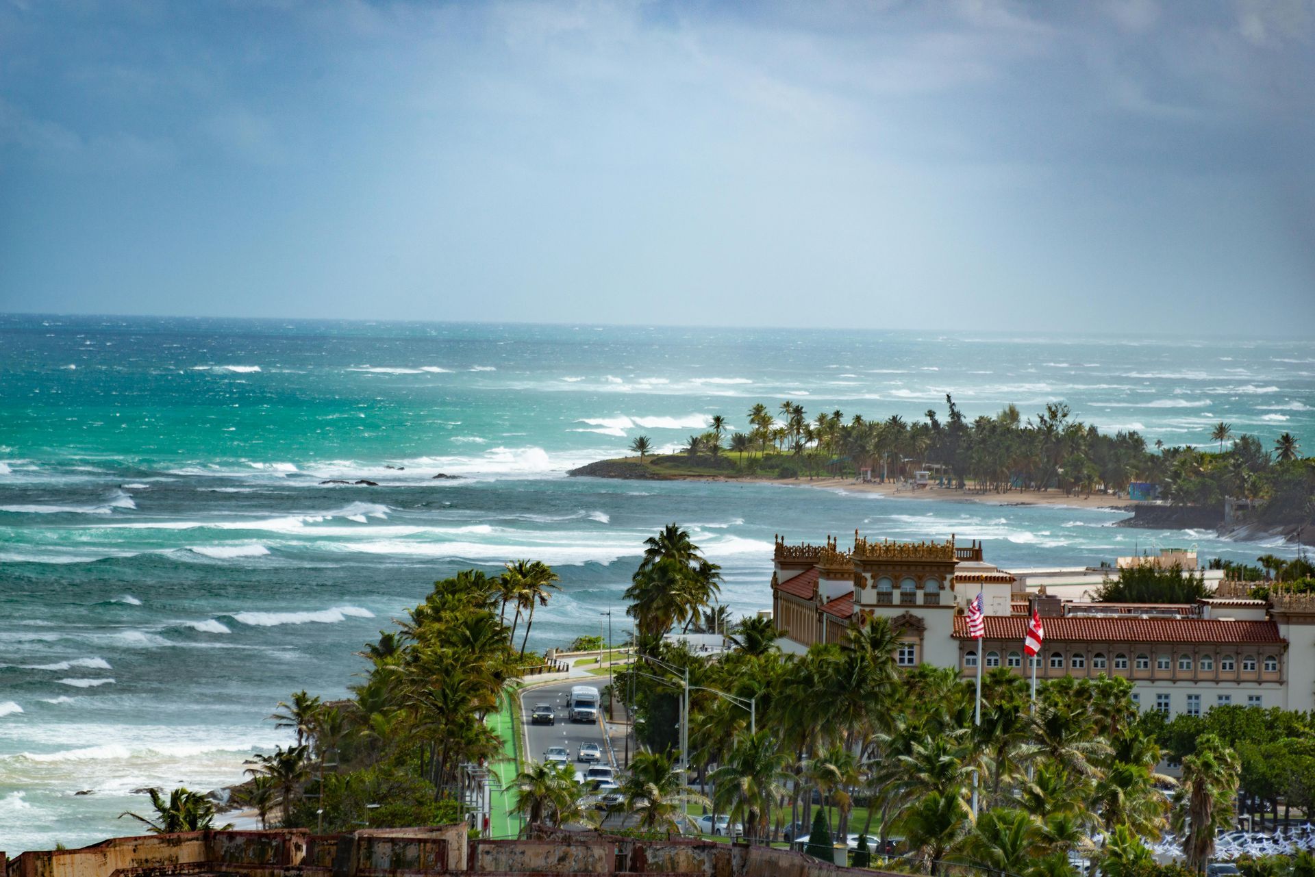 Coastal resort with palm trees, red-roofed buildings, and turquoise ocean  Puerto Rico waves under a hazy sky