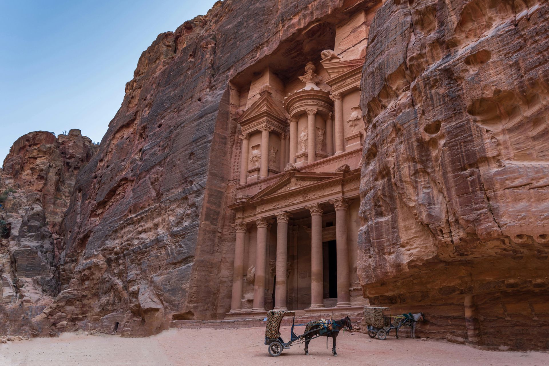 The Treasury at Petra, Jordan, carved into sandstone cliffs, with horse-drawn carriage in front.