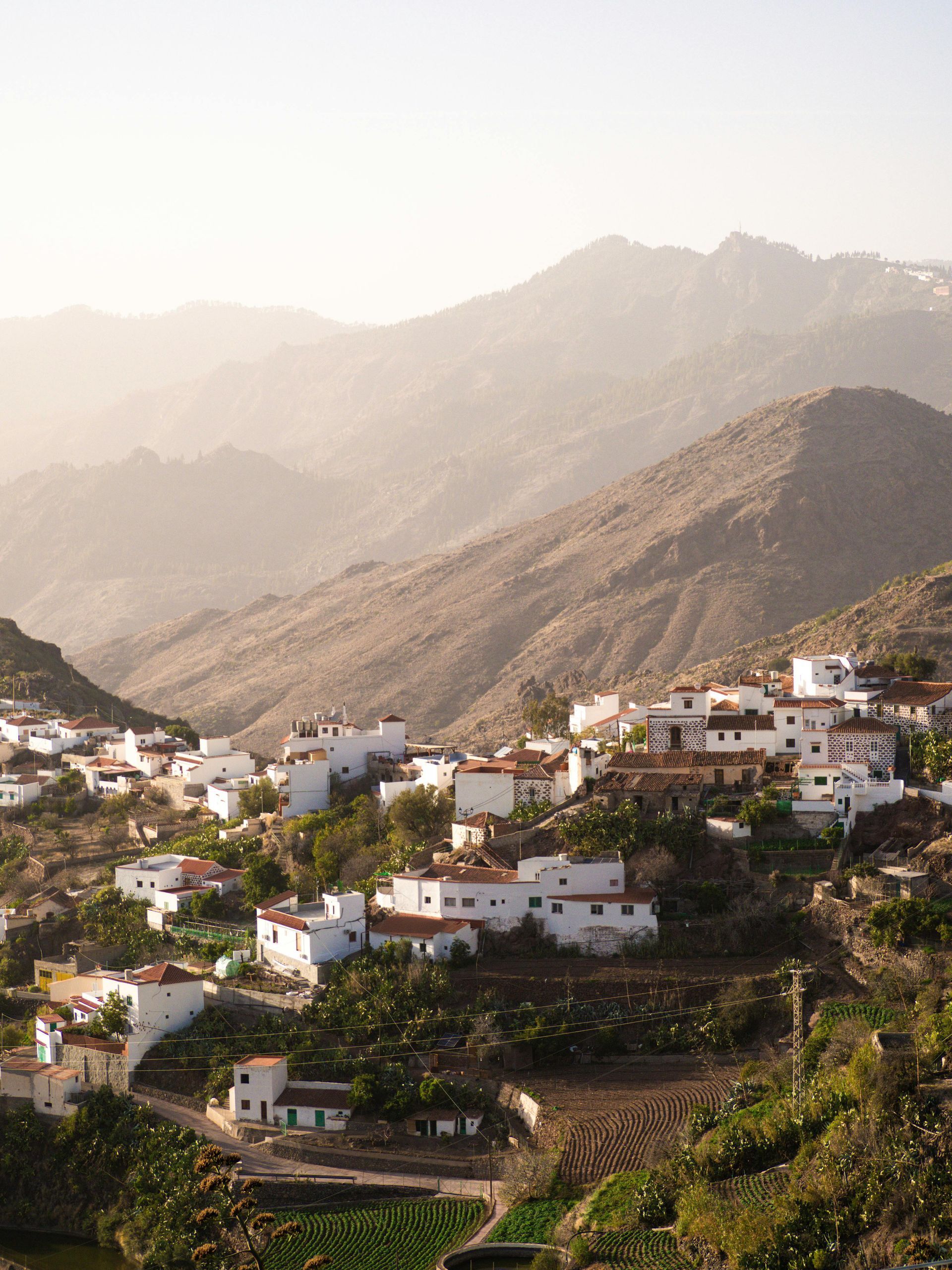 Mountain village with white houses on terraced hills under hazy, rugged mountains
