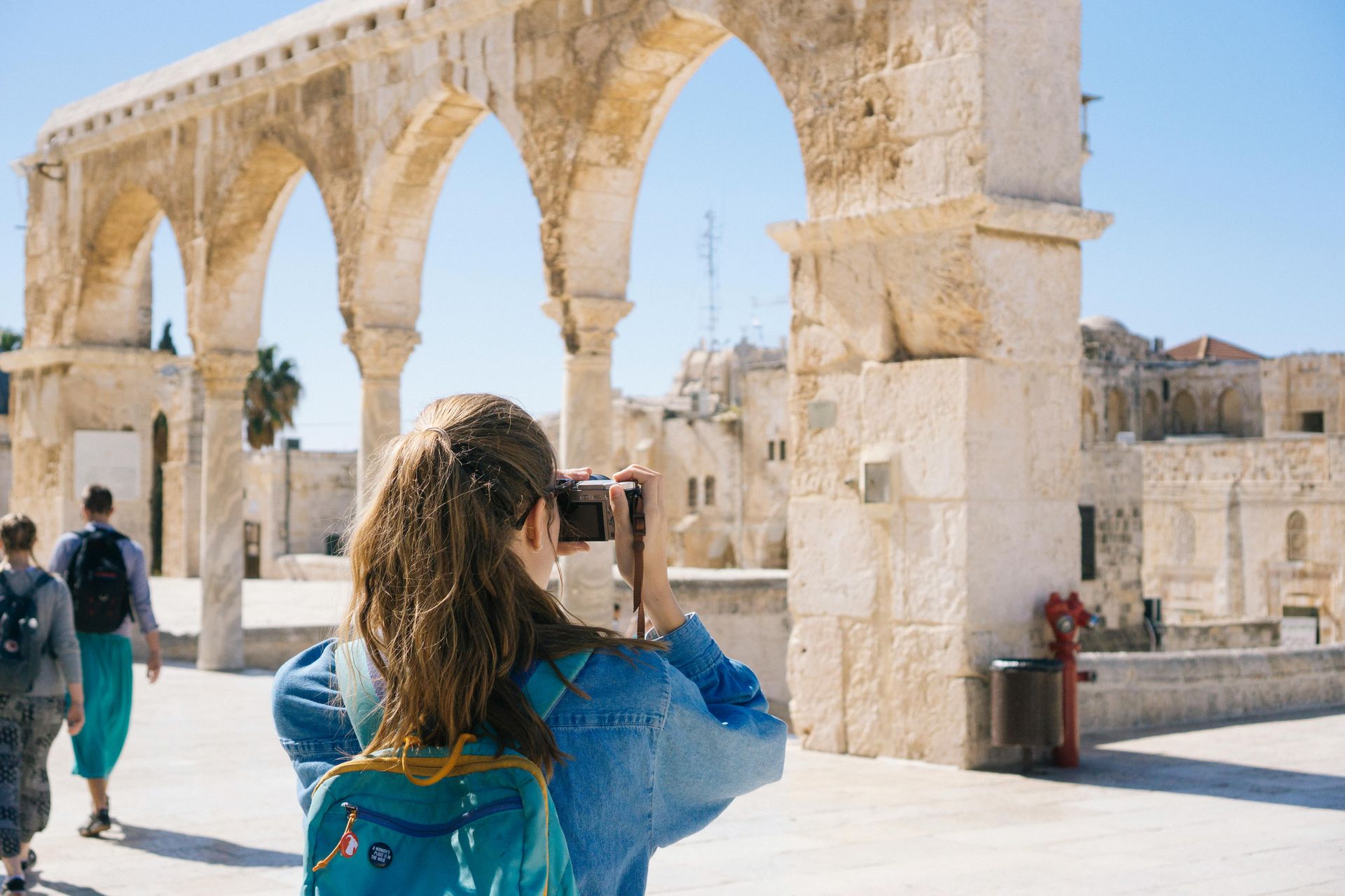 Woman with camera photographs stone arches in a sunlit outdoor setting. Israel