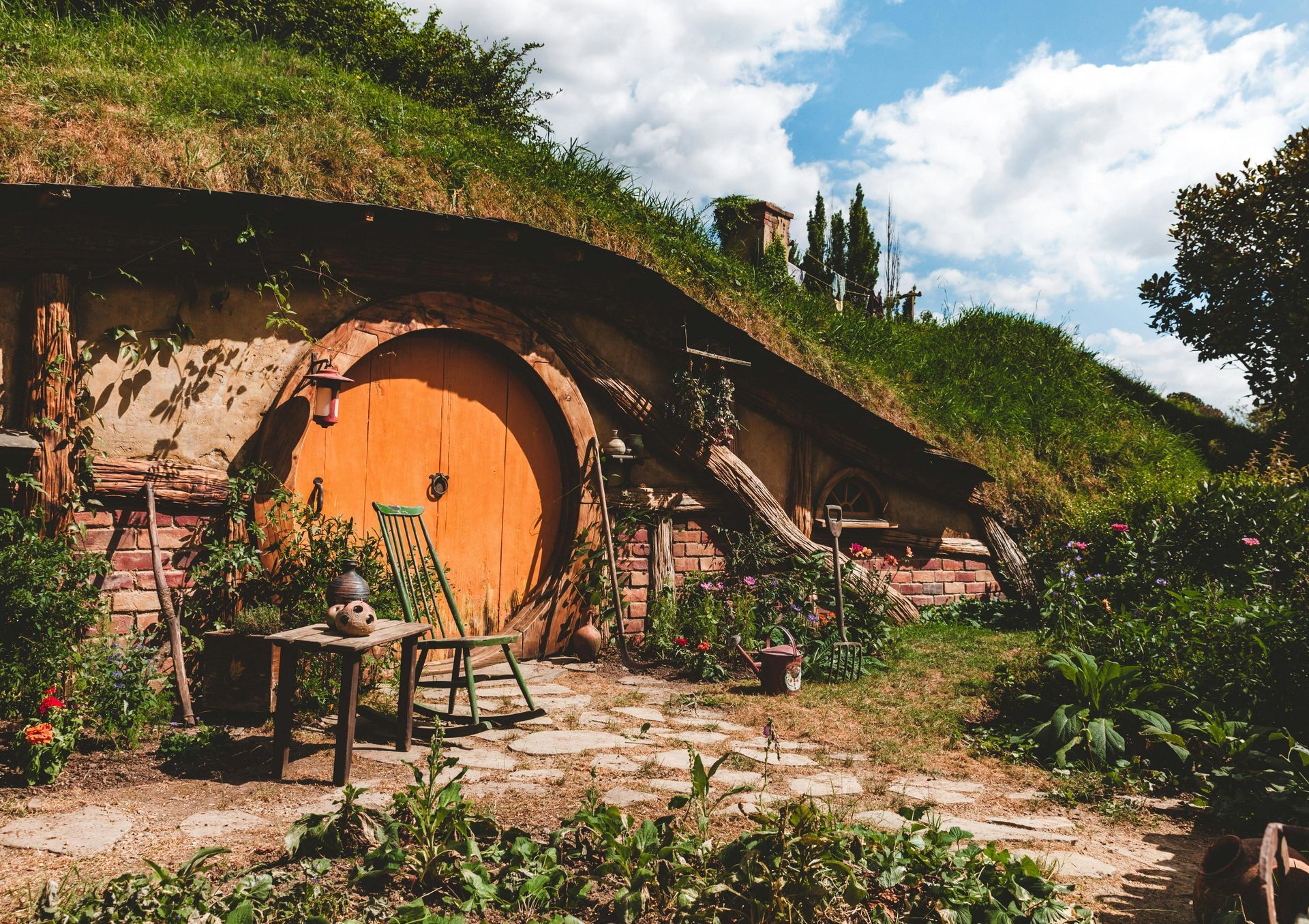 Hobbit hole with round orange door, grassy roof, and small table.