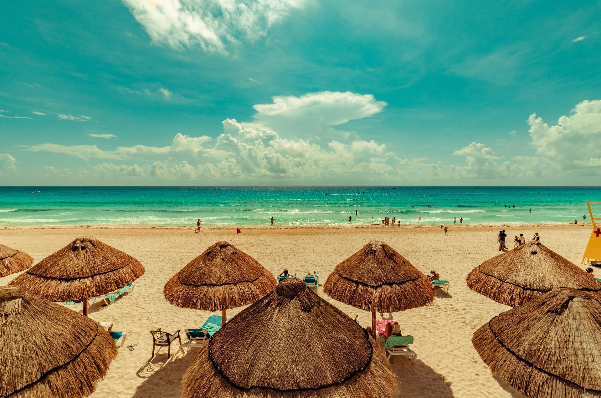 Thatched beach umbrellas on a sandy shore facing a turquoise ocean under a cloudy blue sky