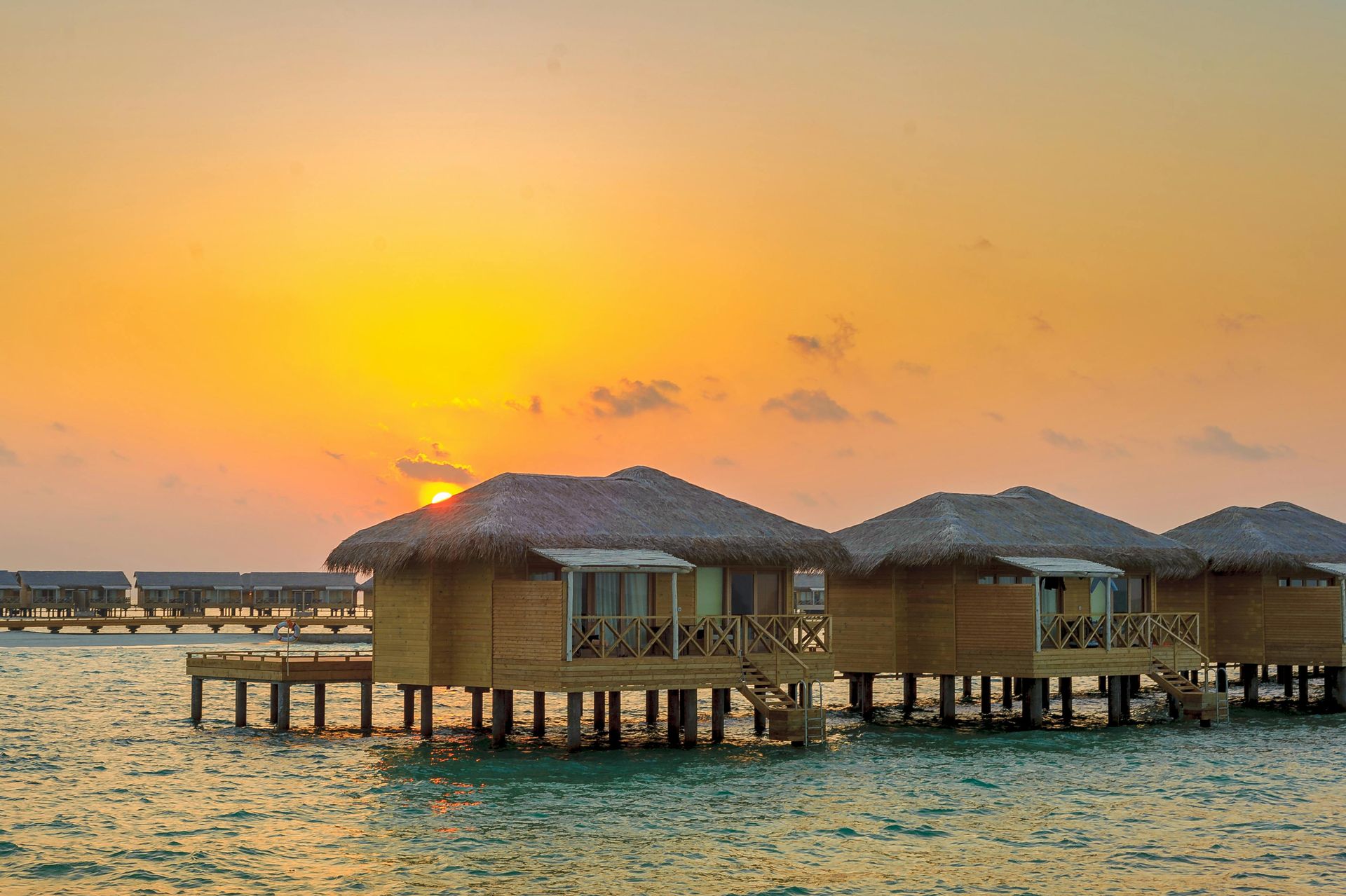 Overwater bungalows at sunset; golden sky reflecting on the ocean.