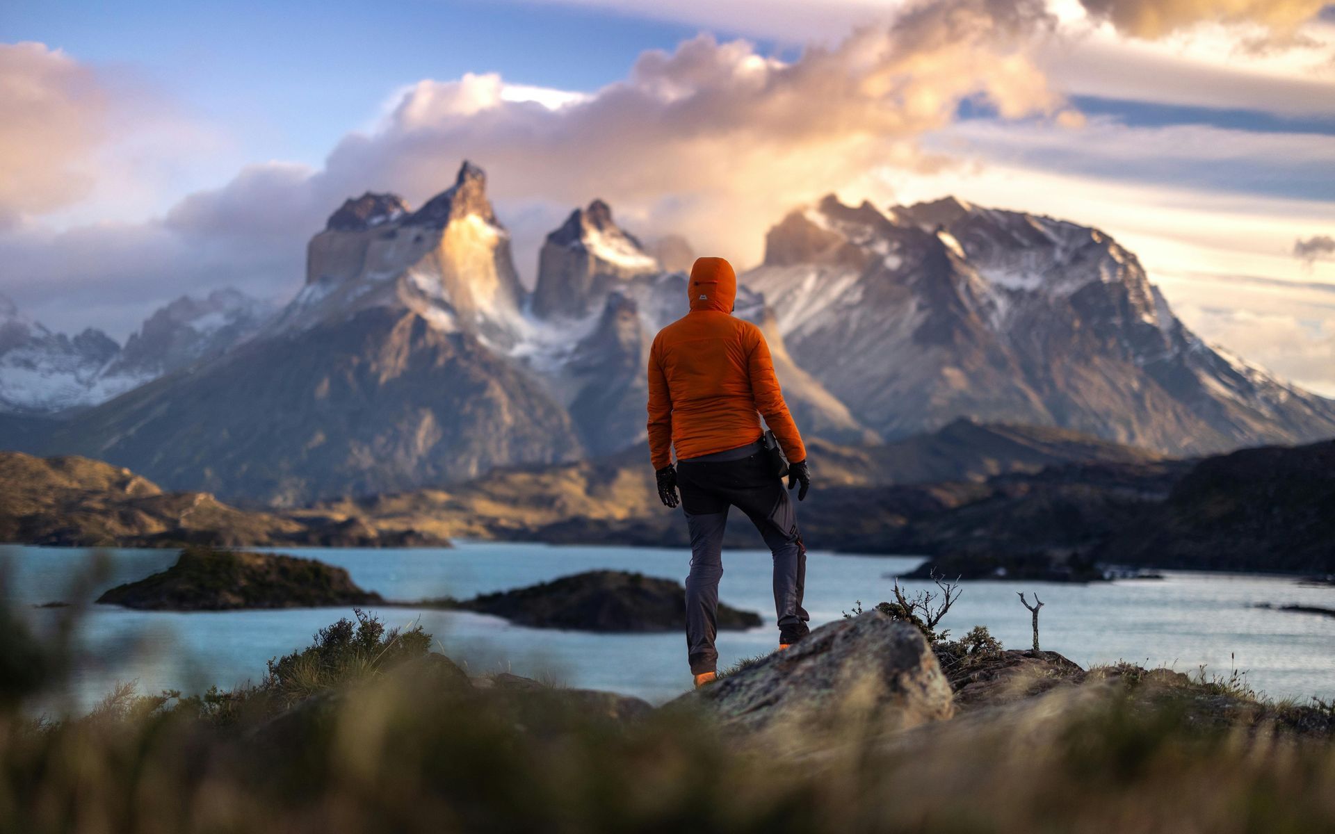 Person in orange jacket looks at snowy mountains and lake. Torres del Paine W Trek
