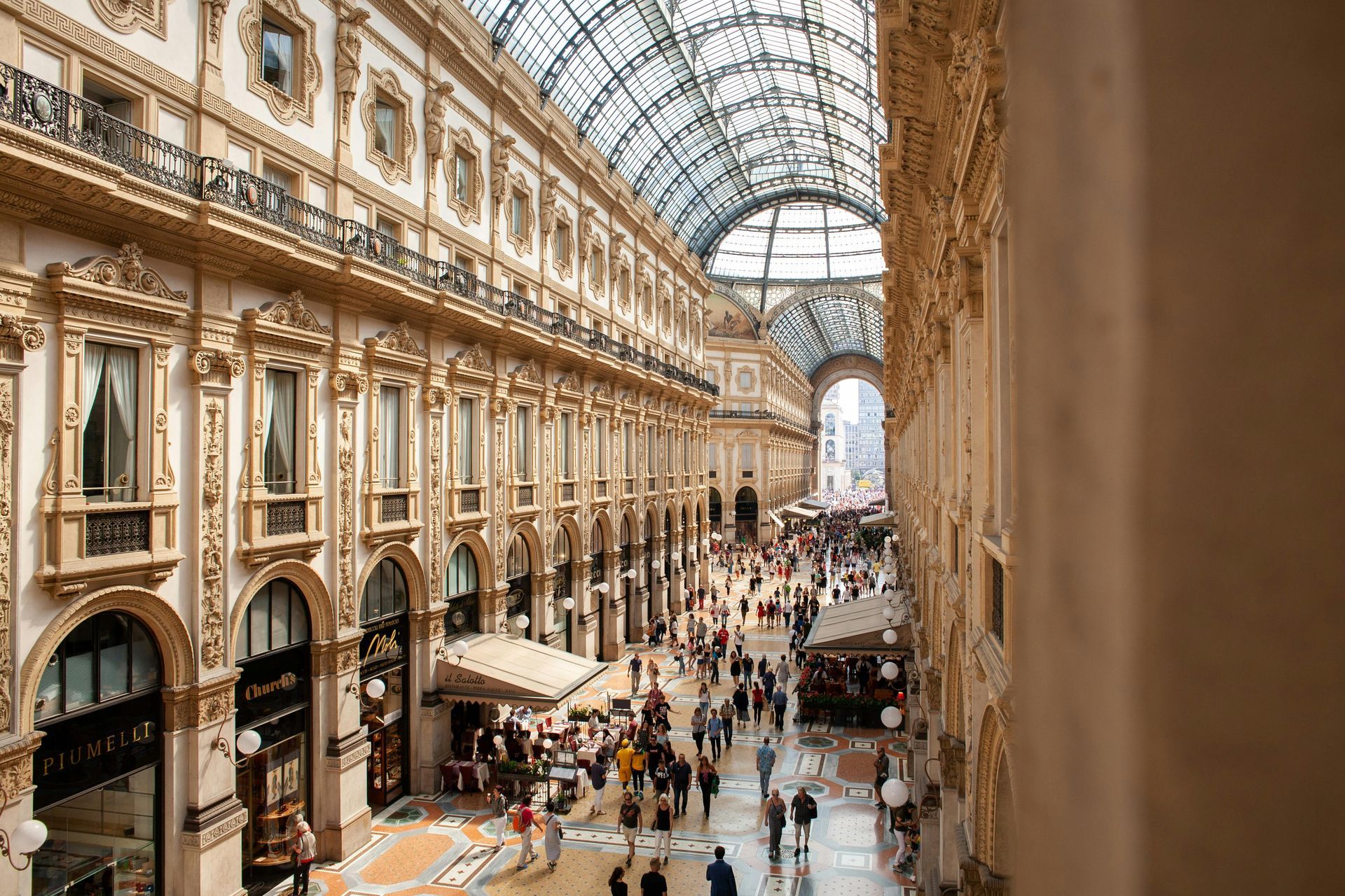 Interior view of Galleria Vittorio Emanuele II in Milan, Italy, with people walking beneath a glass-domed ceiling.