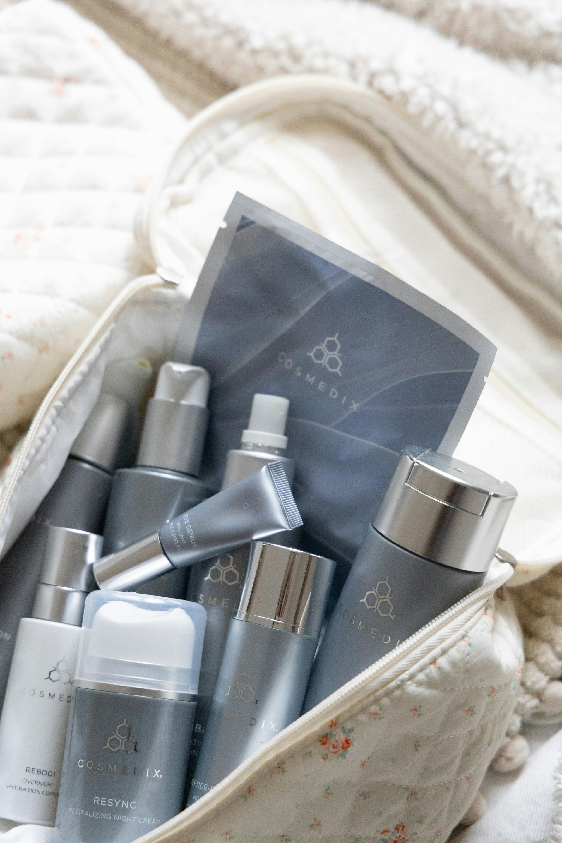 Cosmetic products in a white bag; silver bottles, grey package; soft, white background.