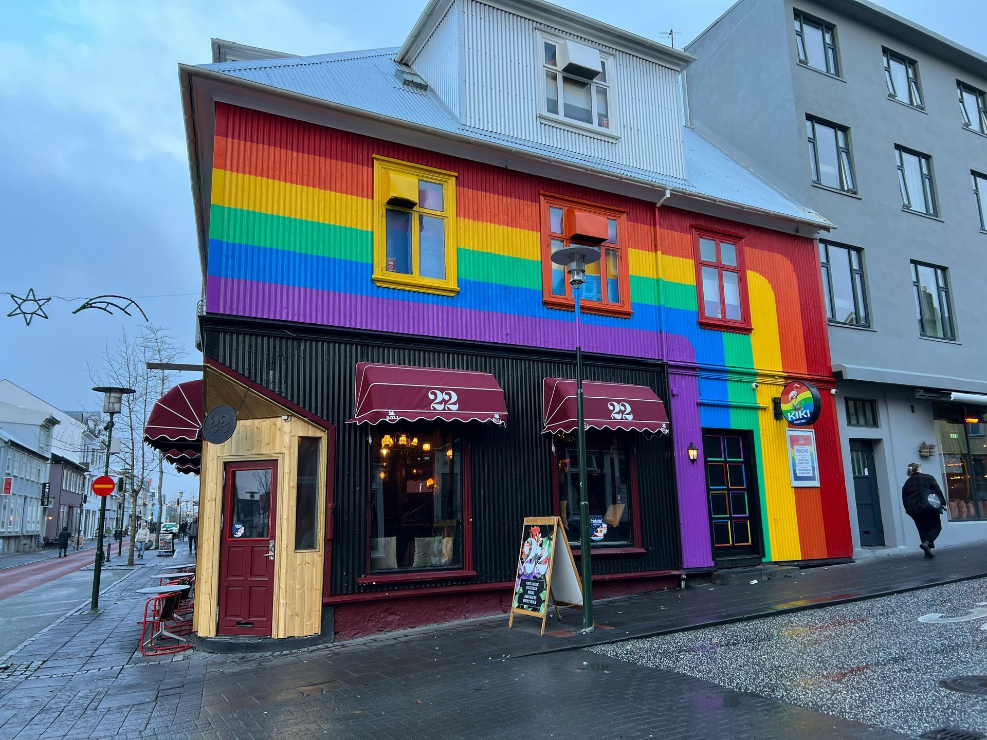 A two-story building in Reykjavík painted with a rainbow mural, featuring black lower walls and a bright red door.