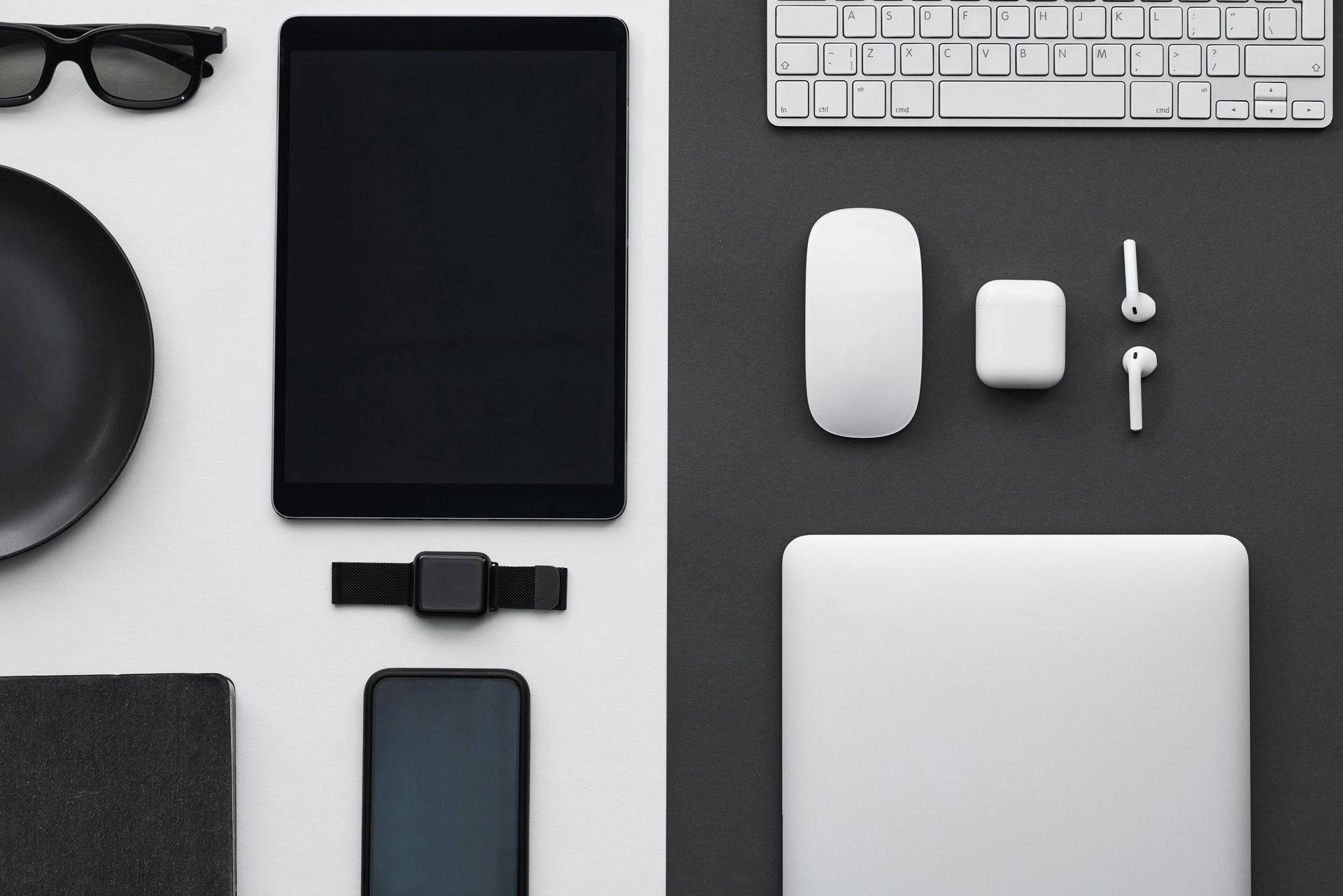 A flat-lay of tech gadgets, divided by color into a black-and-white grid featuring a tablet, laptop, mouse, and accessories.