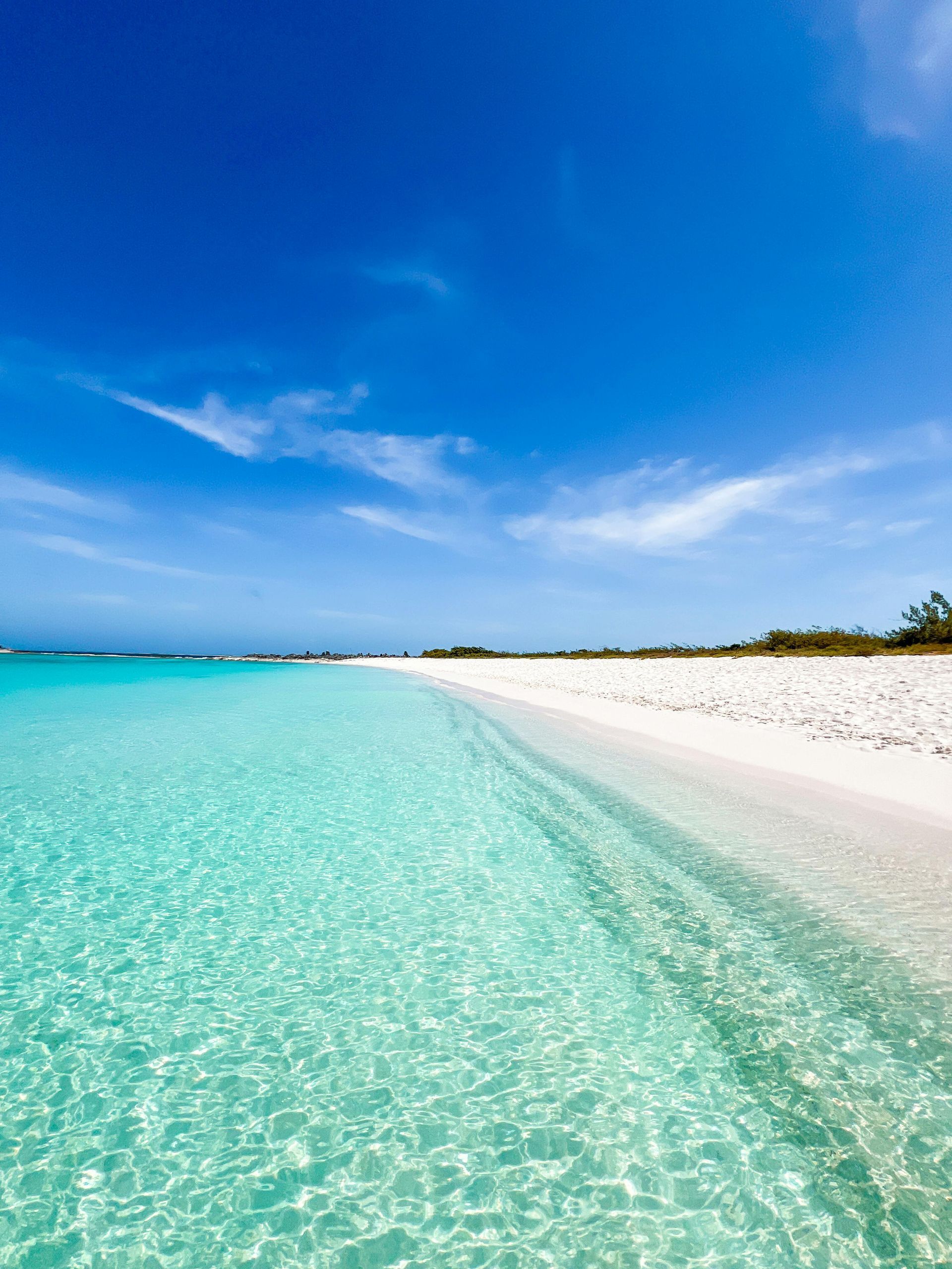 A turquoise ocean meets a pristine white sand beach under a clear, vibrant blue sky.