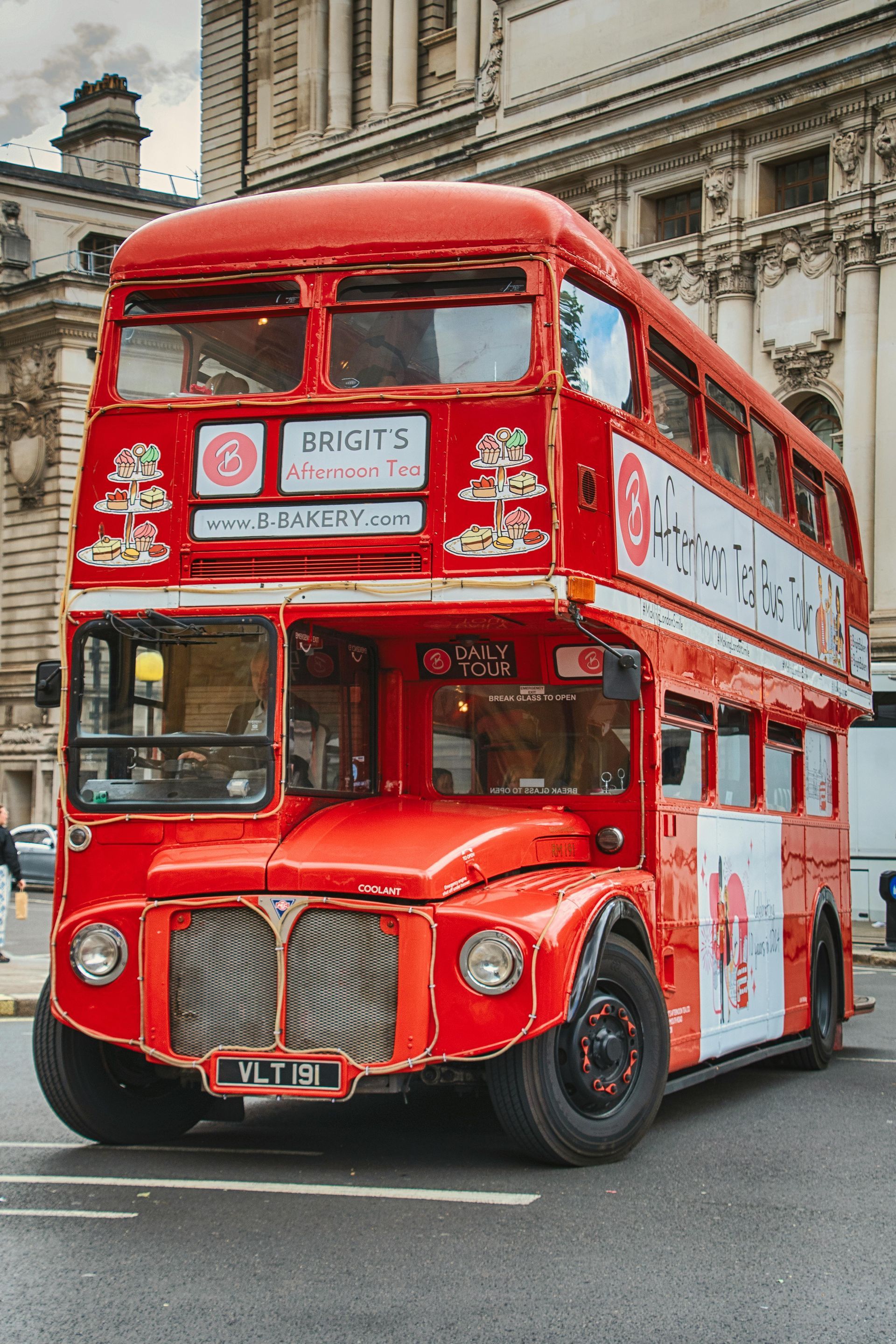 Red double-decker bus parked on a city street; London. The bus has advertisements on its side.