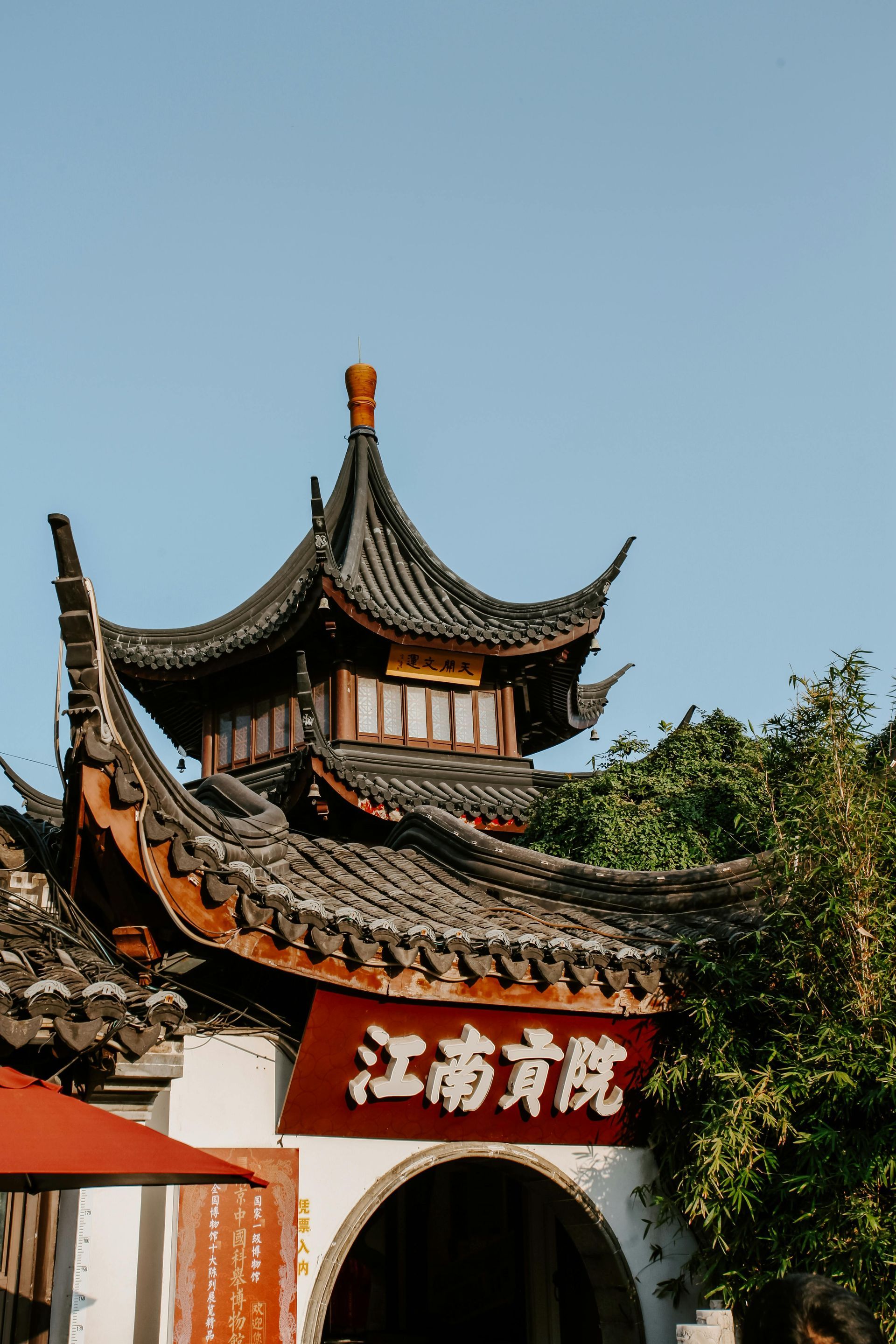 An arched entryway with a red sign featuring white Chinese characters, topped by a traditional tiered pagoda-style roof.