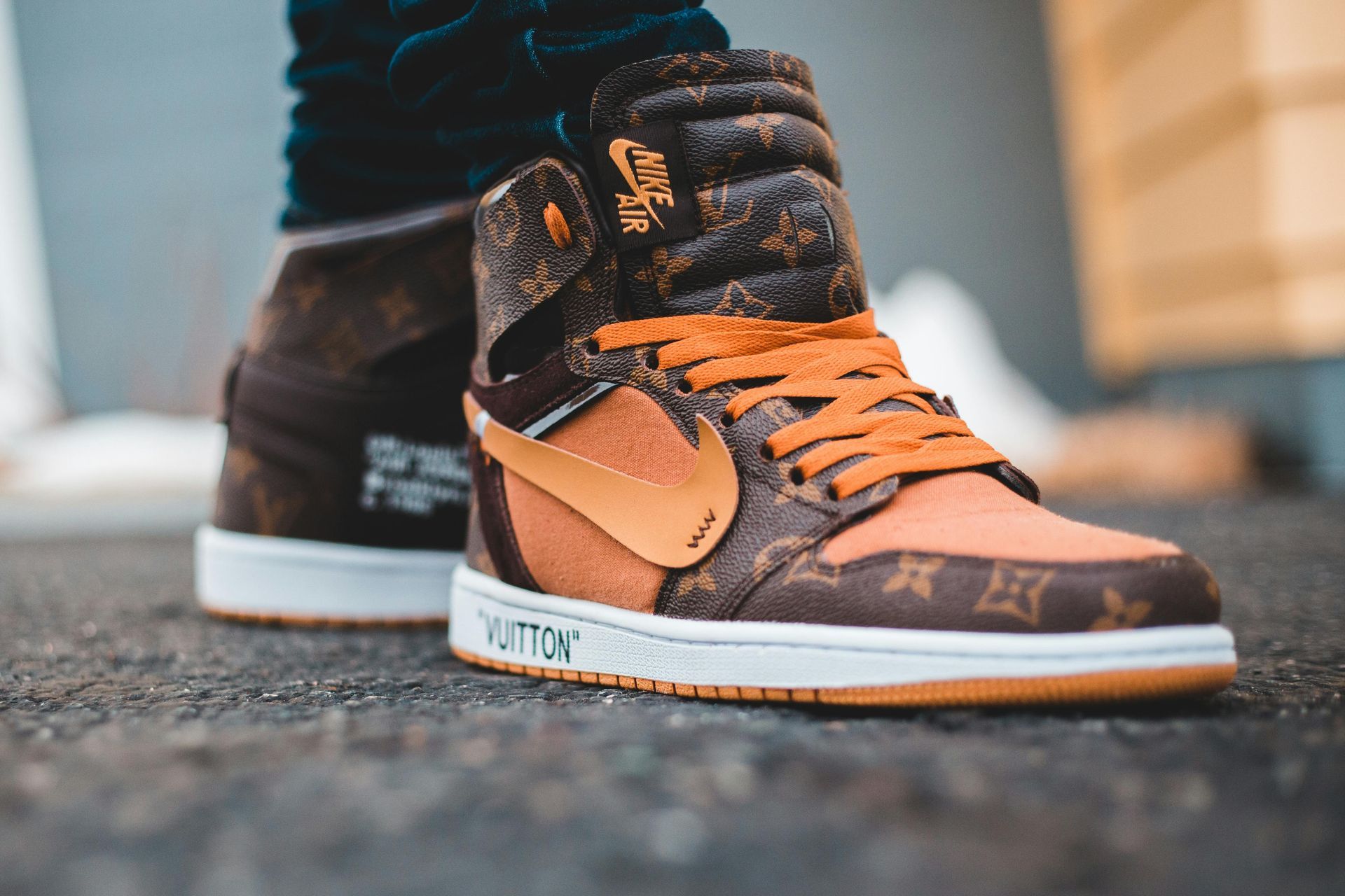 A close-up of a custom high-top sneaker featuring a brown Louis Vuitton monogram pattern, orange details, and