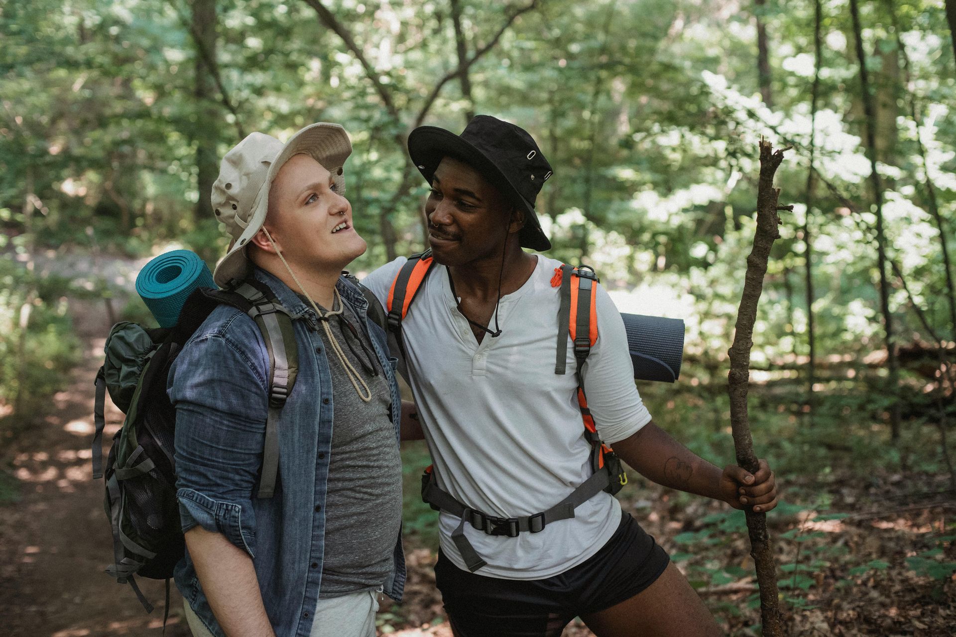 Two hikers on a forest trail, one with a stick, one with a backpack looking upwards.