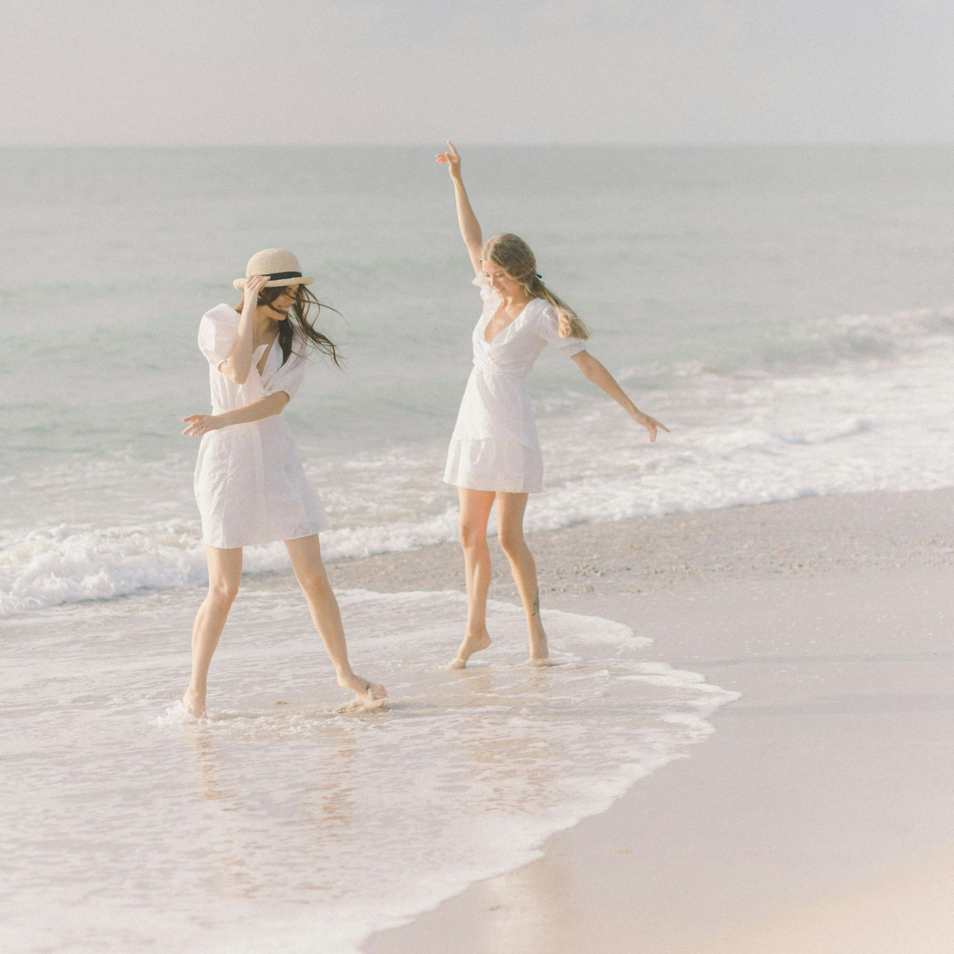 Two women in white dresses are standing on a beach.