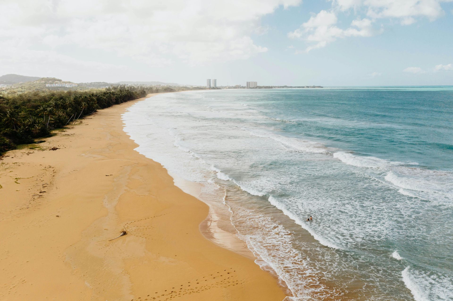 Sandy beach curving beside turquoise waves under a bright, cloudy sky Puerto Rico