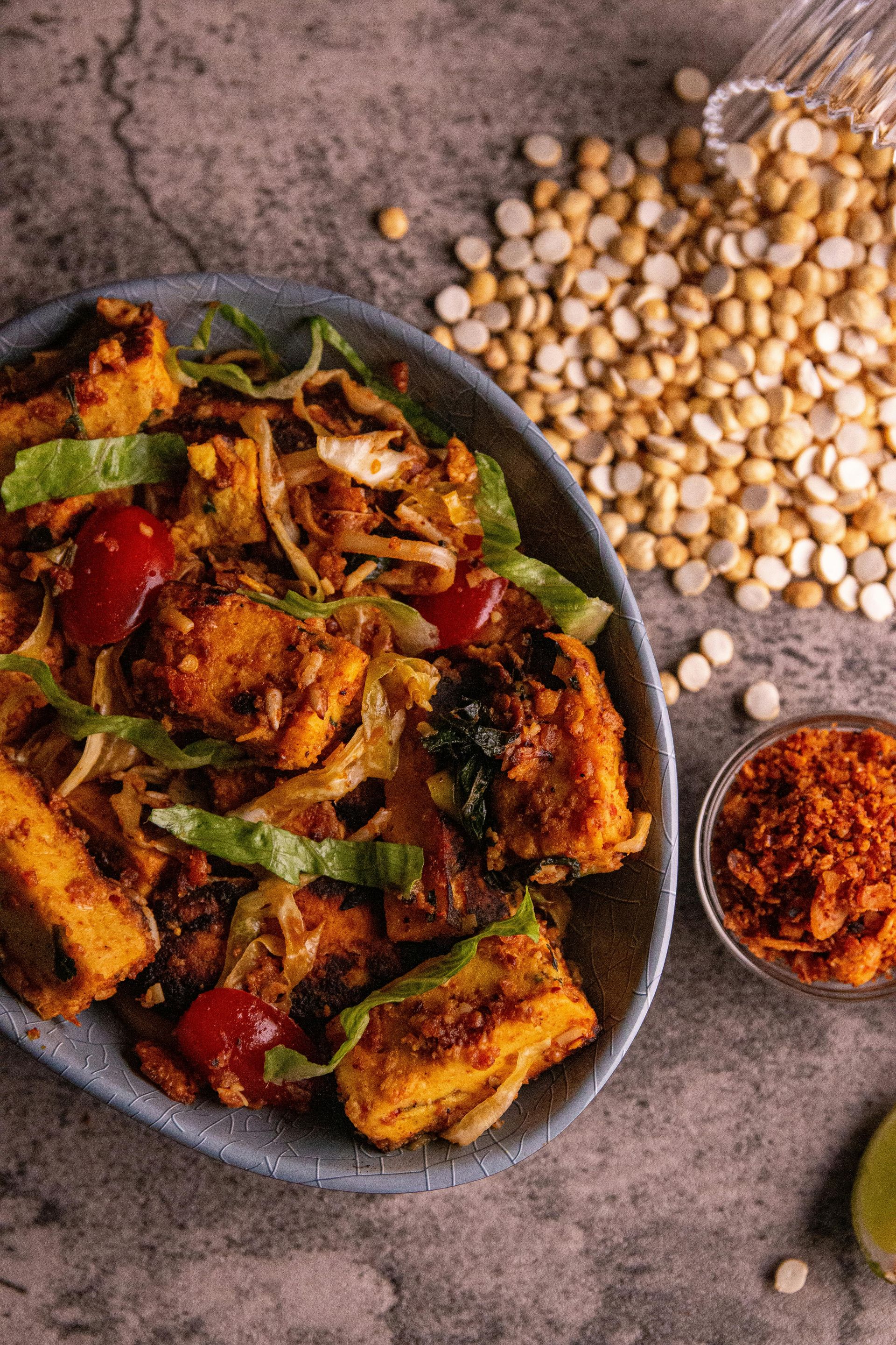 Spicy chickpea curry in a black bowl with fresh herbs, rice, and spices on a rustic table.