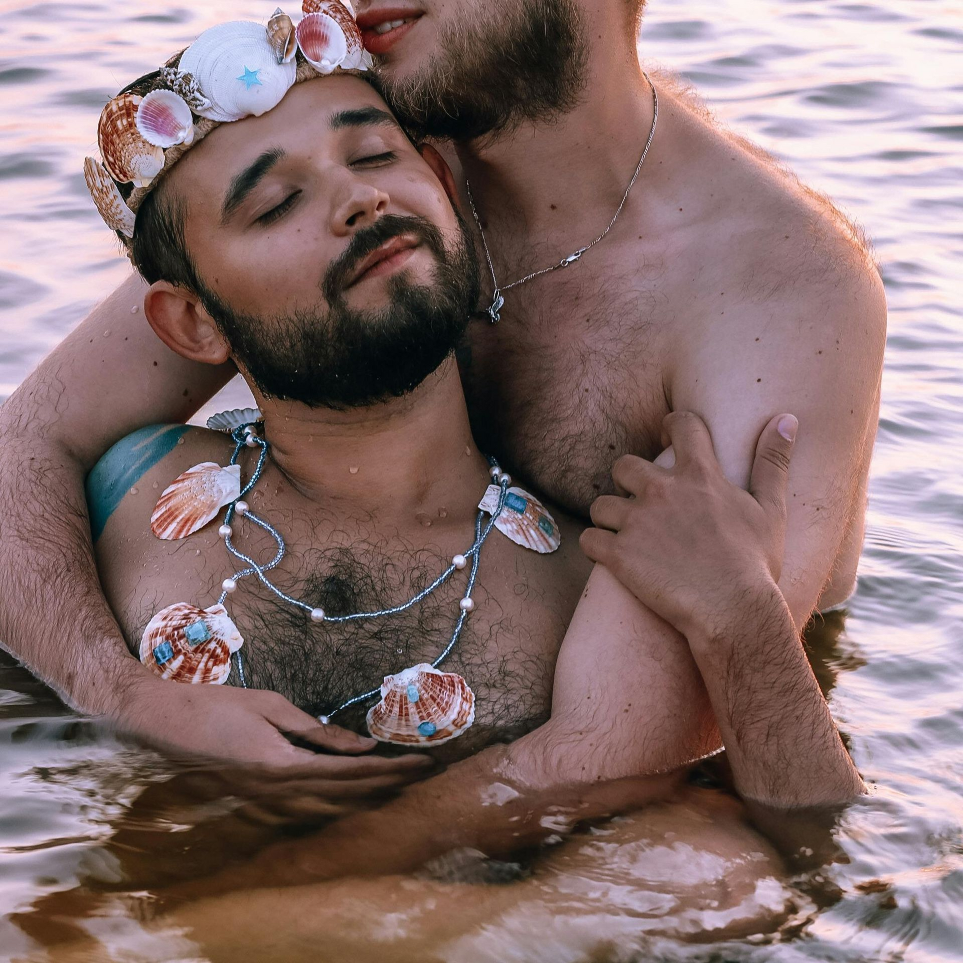 Two men are hugging each other in the water . one of the men is wearing a crown.