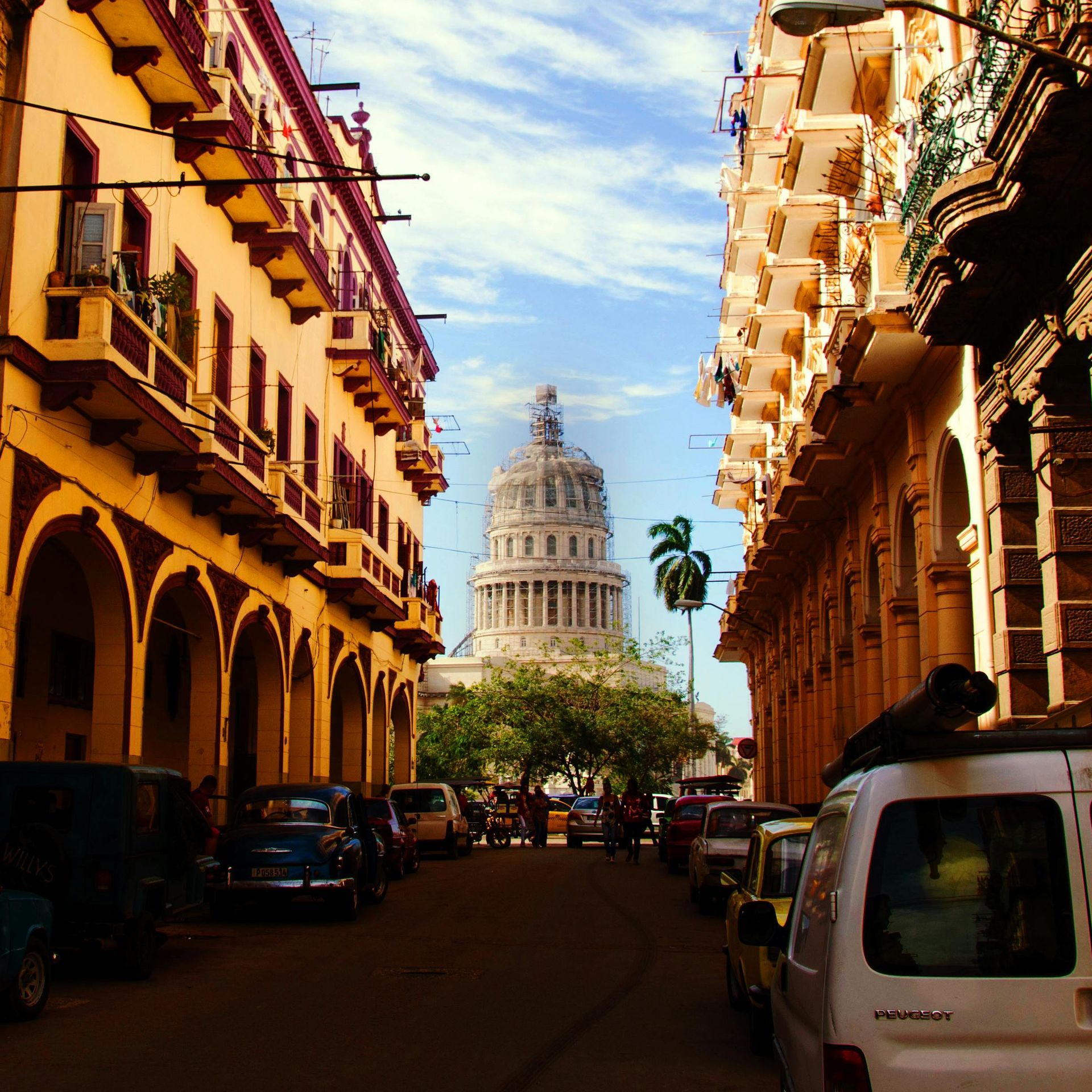 Street view of buildings leading to the Capitolio in Havana, Cuba, with cars and blue sky.