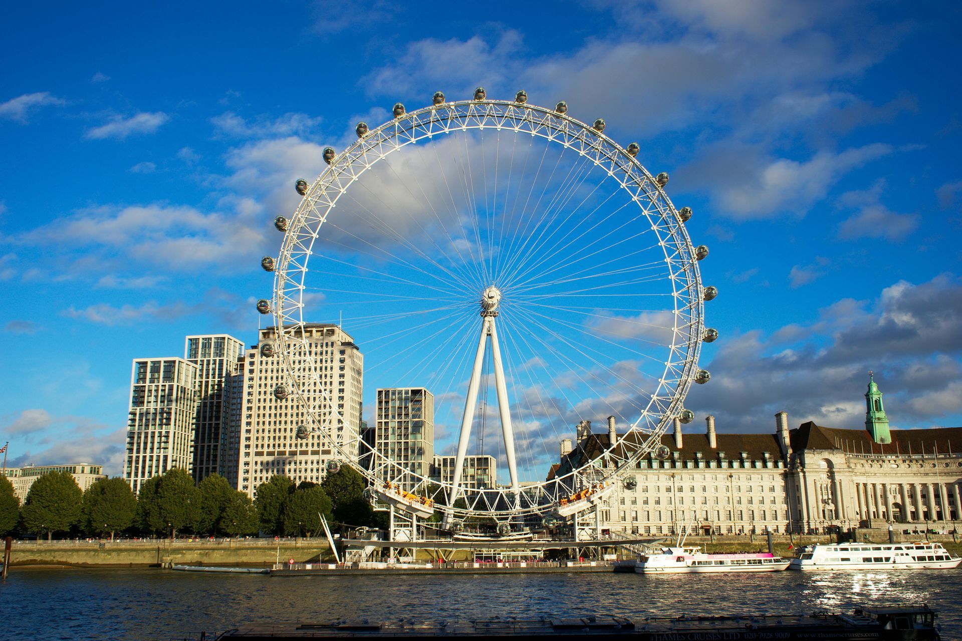 London Eye Ferris wheel on the Thames River, with buildings and blue sky.