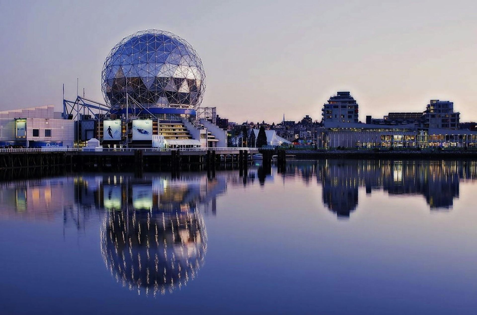 A large geodesic sphere reflecting in calm water with buildings in the background during dusk in Vancouver, Canada.
