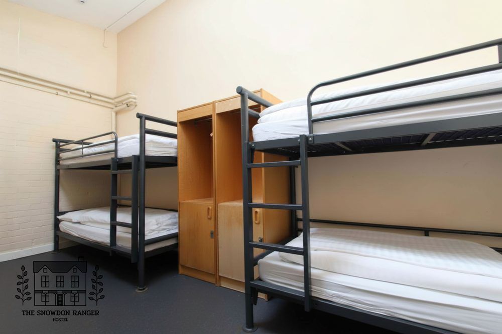 Dorm room with two bunk beds, a wooden wardrobe, and plain cream walls