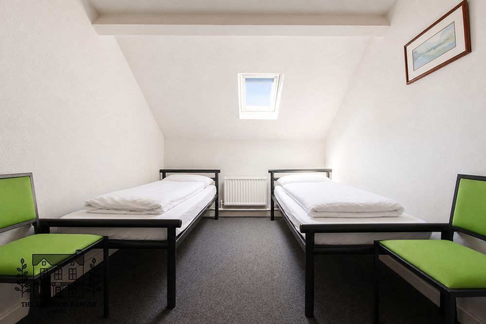 Small twin bedroom with two single beds, green chairs, white walls, and a skylight window.