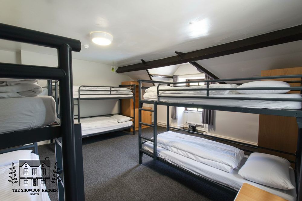 Dorm room with four metal bunk beds, white bedding, and carpeted floor