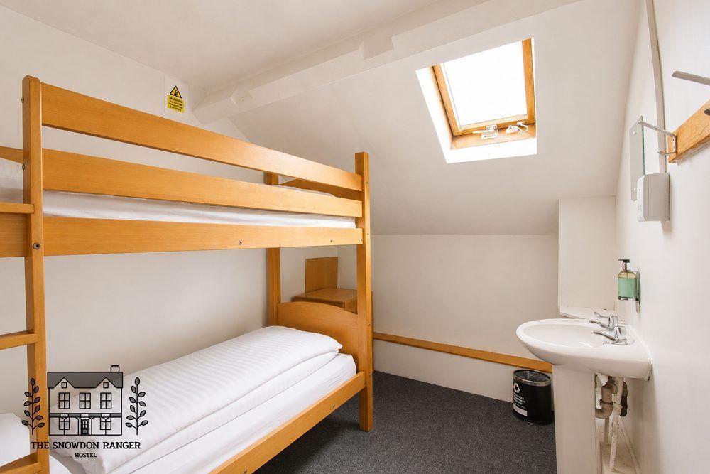 Small attic bedroom with wooden bunk bed, skylight, white walls, and a wall-mounted sink