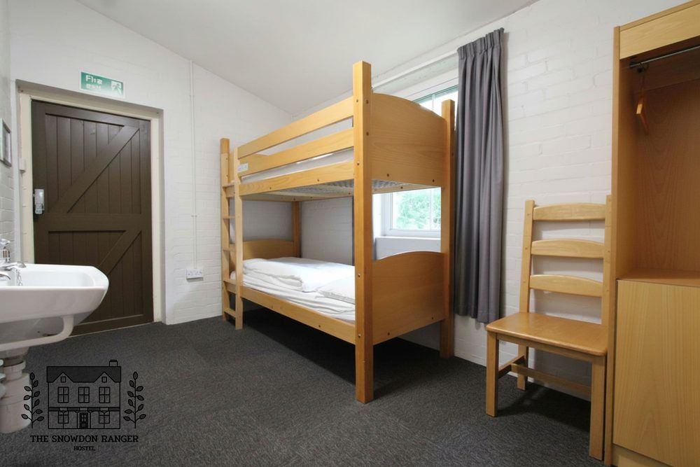 Small dorm room with bunk beds, single bed, sink, and brown doors on carpeted floor.